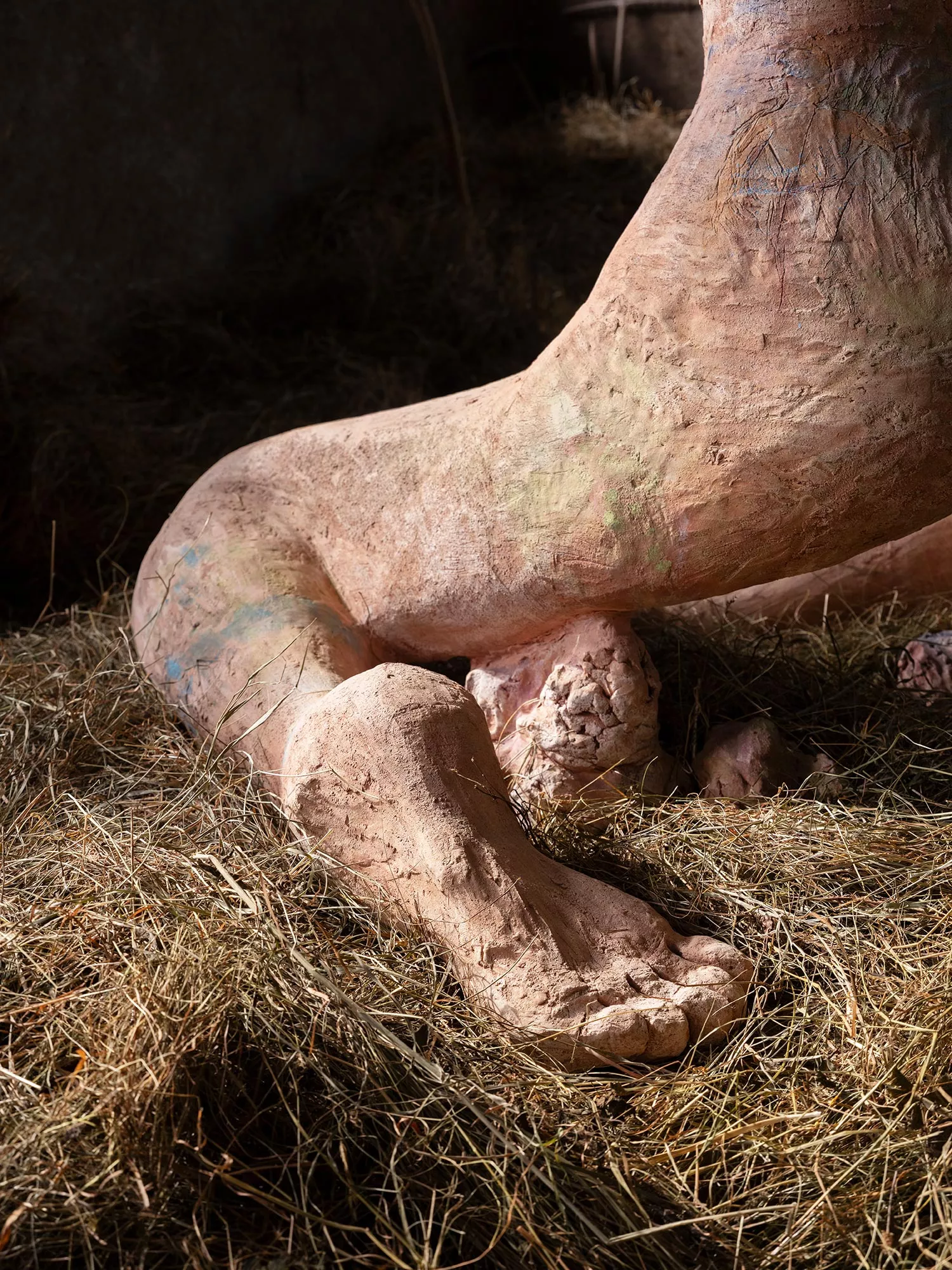 Gaia Fugazza - Gaia Fugazza, Mother of Millions, 2025, close-up of the sculpture’s textured foot, with the leg visible behind it, surrounded by hay.