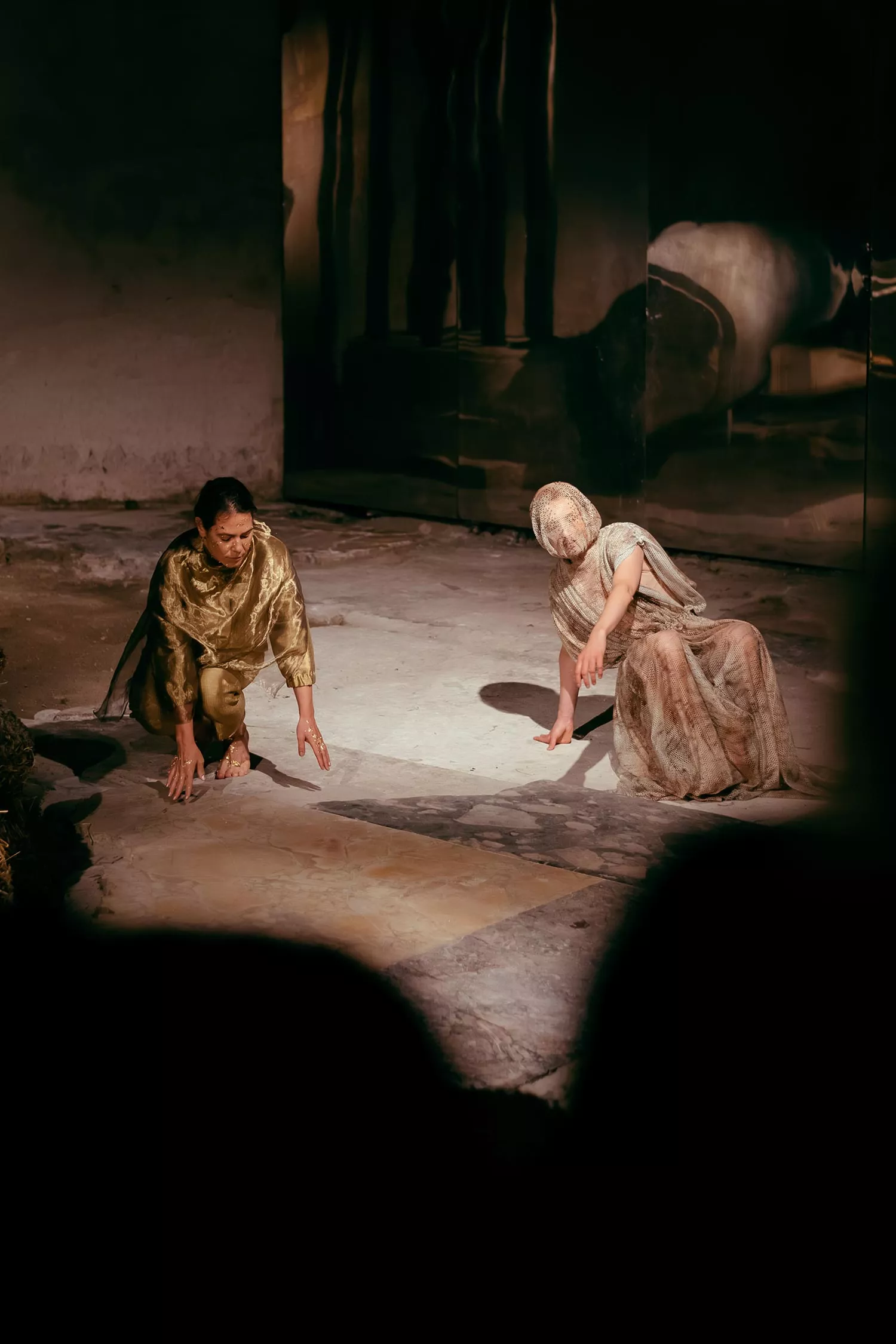Gaia Fugazza - Gaia Fugazza, 2024, Farewell to Known Skies. Two performers crouch on the floor in a rustic, dark setting. 