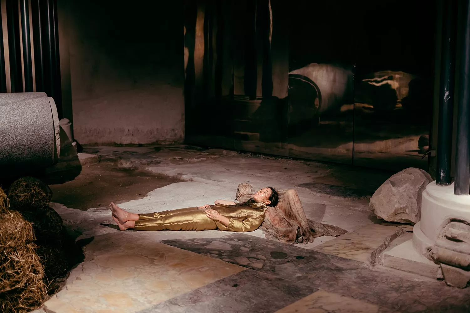 Gaia Fugazza - Gaia Fugazza, 2024, Farewell to Known Skies. Two performers lie at the centre of a stone floor in a dark, rustic space.